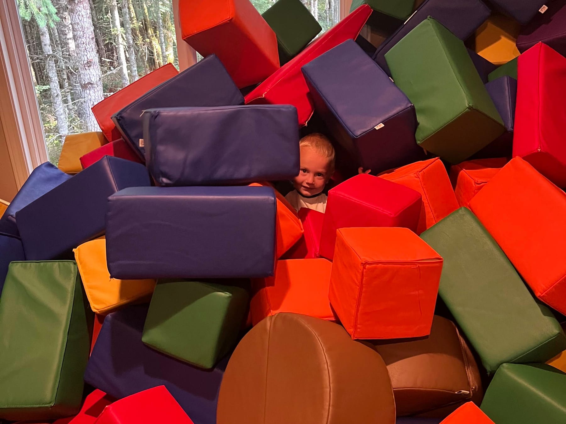 A child peeking out from a pile of soft blocks